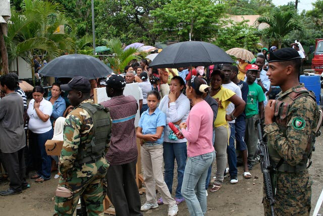 Maj. Wendy Rodgers for Wikimedia Commons.  Image shows Dominicans and Haitians lined up in the rain holding umbrellas to see medical providers from the U.S. Army Reserve in Jaibon, Dominican Republic.