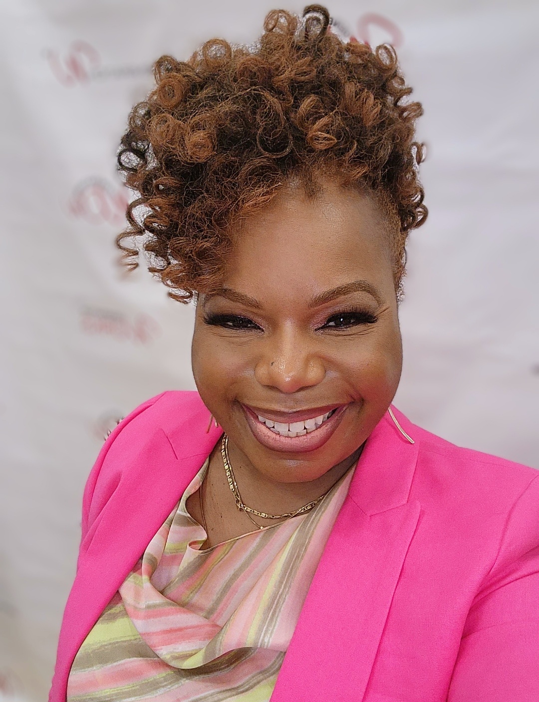 diya wynn wearing a pink blazer and striped colorful top smiling at the camera